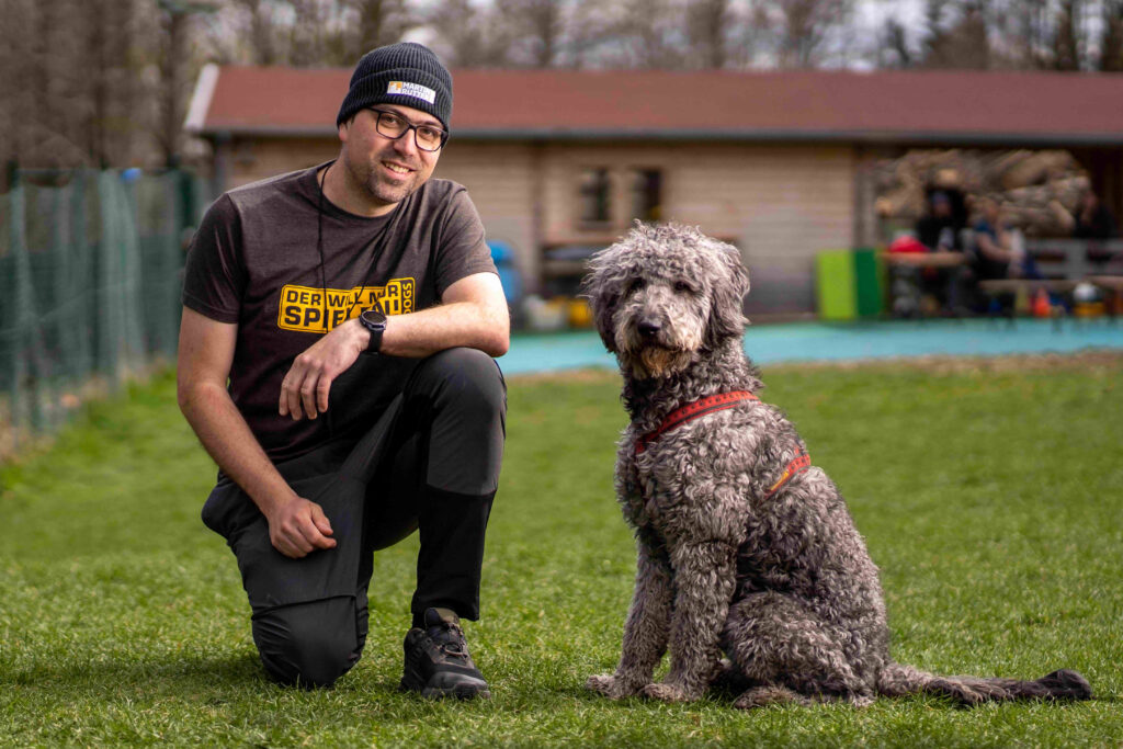 DOGS Trainer Christian Pirkheim sitzt mit seinem Golden Doodle auf unserem Trainingsgelände Dornegg