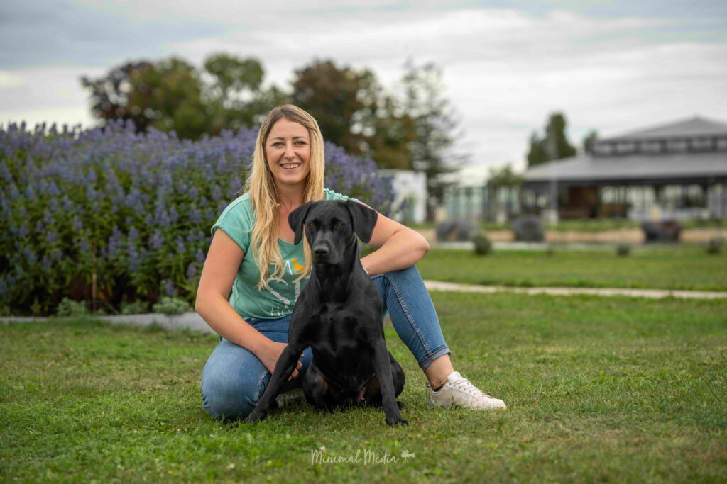 Hundetrainerin Lena Reinisch sitzt mit ihrer Labradorhündin vor einem Lavendelbusch im Pro Village