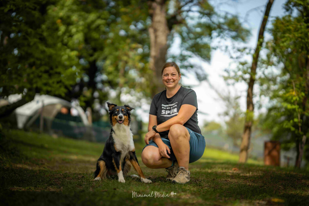 DOGS Trainerin Tina Mairold sitzt mit ihrer Australian Shepherdhündin Izzy auf einer Wiese