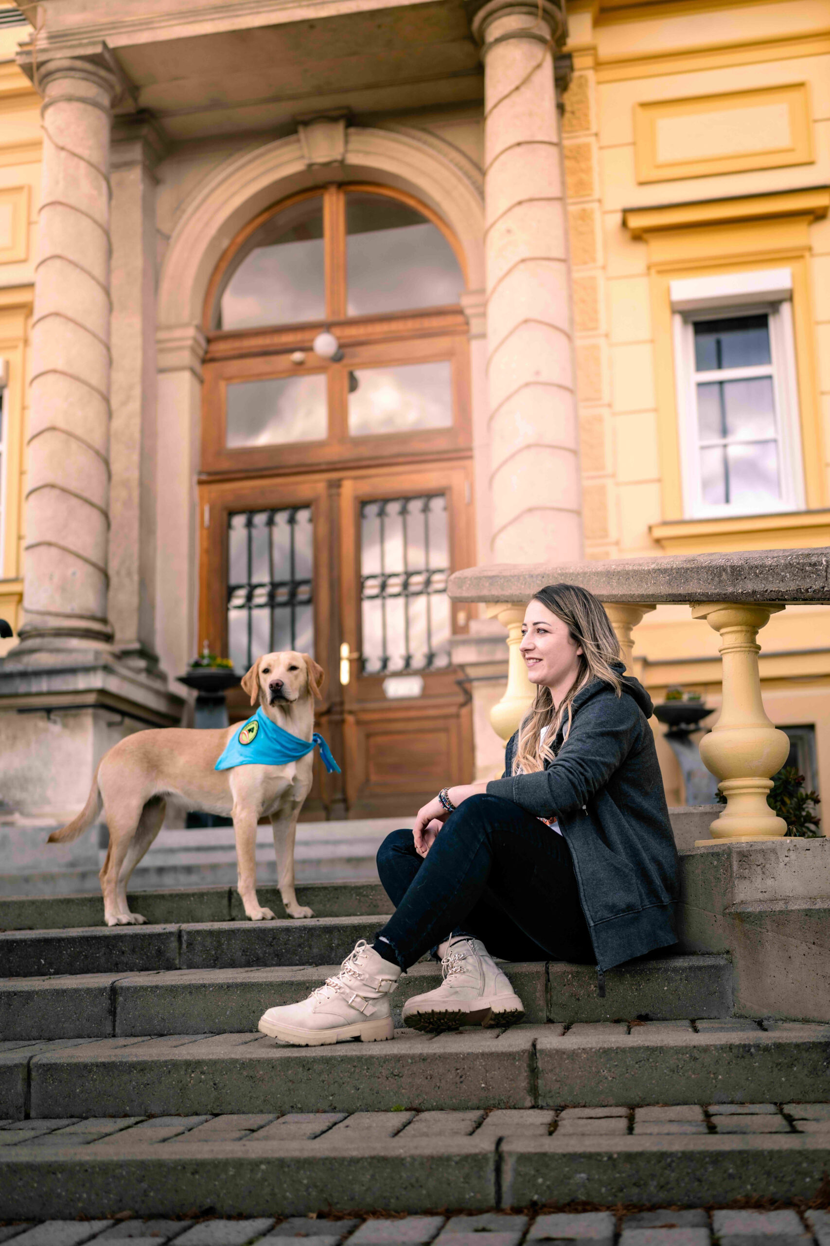 Therapiebegleithund in Ausbildung mit Halterin vor einem Gebäude im Außenbereich